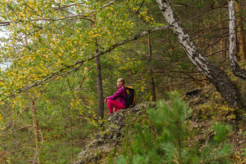 young woman hiker sits resting on a cliff among a mountain forest