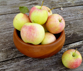 Apples. Bunch of freshly picked green apples with red stripes packed into wooden bowl on old rustic wood background. Close up, selective focus.
