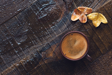 Fototapeta na wymiar Cup of black coffee and autumn leaves on old wet wooden table. Flat lay