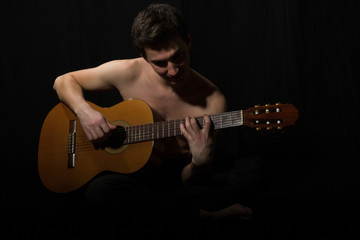 Obraz premium Handsome young musician playing on guitar. Naked torso. On black background.