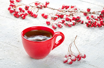 Red cup with coffee and branches with hawthorn berries on old white wooden table. Selective focus.