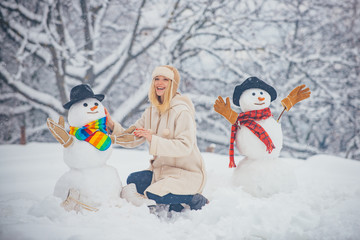 Funny Santa girl posing on winter weather. Girl playing with snowman in winter park. Merry Christmas and Happy Holidays. Making snowman and winter fun for girl.