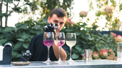 Bartender making alcoholic cocktail, summer cocktail outdoors. Colorful cocktail on top of the bar. Summer refreshment drinks.