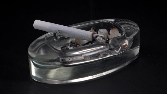 White cigarette burning in ashtray on black background. Time lapse. Isolated.