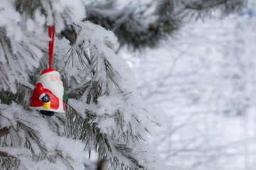 New Year. Christmas and decorations. Toy Santa Claus swinging on a branch in the forest. Snowing