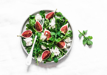 Figs, goat cheese, arugula salad on light background, top view. Delicious breakfast, snack, appetizer, tapas