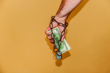 Man's hand is wrapped in a chain, holds dollars. The concept of monetary and financial dependence.