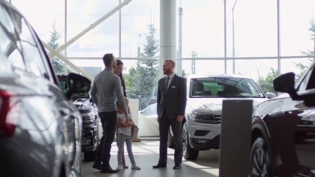 Cheerful car dealer shaking hands with male customer and talking with his wife and little daughter after making successful deal in auto showroom