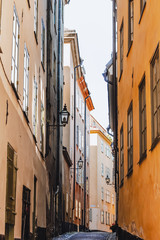 Fototapeta na wymiar Stockholm narrow street. Orange, yellow houses and street lights. View from below of a cozy narrow medieval street yellow orange red buildings facades in Gamla stan, Old Town of Stockholm, Sweden