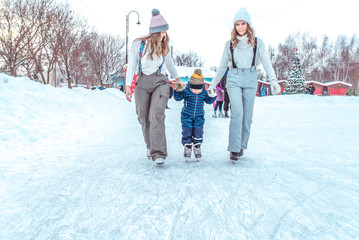 Fototapeta na wymiar Mom with child, a boy 3-5 years old, girlfriend woman, skate in winter in city on rink, ice skating. Happy smiling children play having fun weekend first steps of child ice skating.