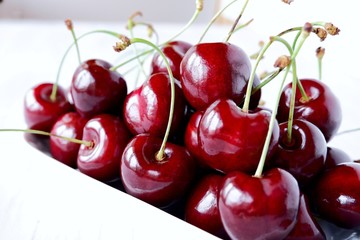 Fresh juicy sweet dark red sweet cherry in a white ceramic bowl on a light wooden background. The concept of a healthy breakfast, a snack. Closeup with selective focus.