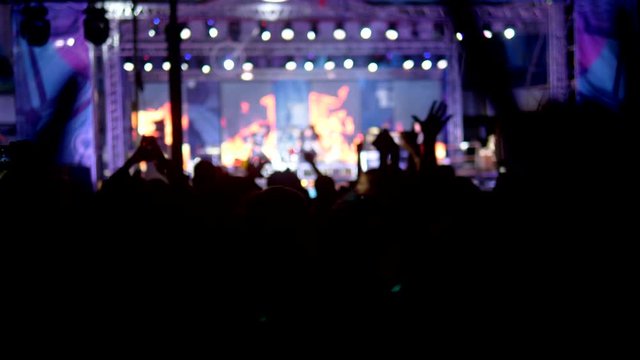 rock concert in the evening. people in the crowd raise their hands and applaud.