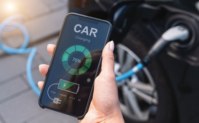 Woman Charging Electric car with Cable Looking at App On Mobile Phone. Close up of smartphone screen. Hand holding smart device. Mobile application for eco transportation. 