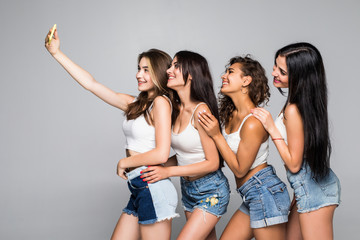 Fototapeta premium Selfie. Happy smiling young four girls taking selfie on the phone isolated on white background.