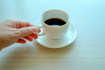 Female hands holding cups of coffee on wooden table background