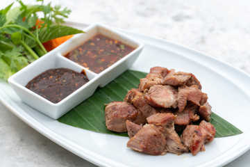 Tasty slice grilled pork, spicy dipping sauce and vegetable side dishes on the white plate.