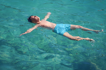 Schoolboy enjoying his summer vacations, he is floating in the clear blue water in form of sea star.