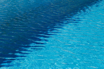 Fototapeta na wymiar A two colored light and dark blue water with ripples and sunny reflections in a swimming pool.