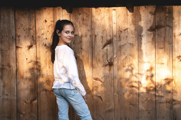 Cheerful cute girl with brunette hair in casual clothes looking over her shoulder at the camera isolated over wooden background