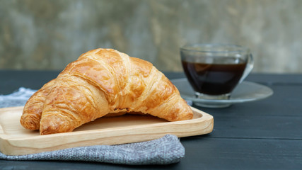 Croissant and black coffee on a black wooden table.