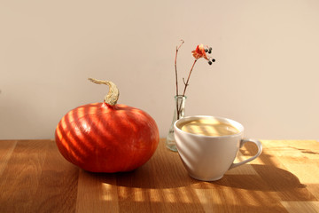Autumn still life on the table with a beautiful light, a glass bottle and a branch, a cup cappuccino