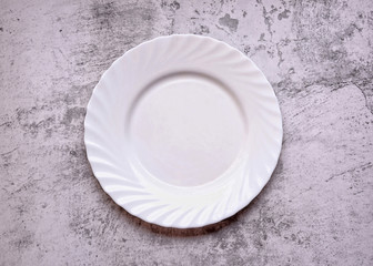Empty white plate on a table. Gray cement background. Top view. Space for a text.