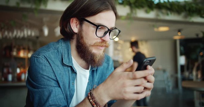 Bearded male hipster in casual clothing browsing internet on smartphone, replacing real communication with online messenger