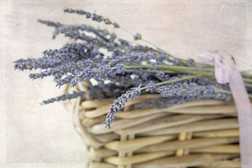 Original textured still life photograph of stems of lavender lying in a basket with a lavender ribbon
