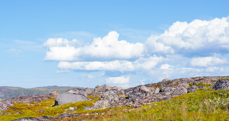 Huge rounded stones on backdrop of hills, small mountains and low Northern the sky. Over stones, hills and grass smoothly move huge white clouds