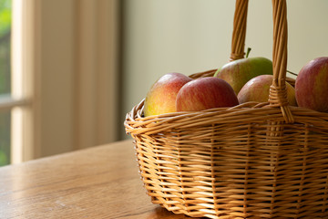 Wicker basket full of fall red and green apples on a table with a shallow depth of field