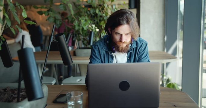 Handsome focused freelancer in denim shirt working on laptop in cafe, coworking space, modern life