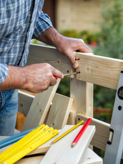 Adult carpenter craftsman with screwdriver screw the screw to fix the boards of a wooden fence. Housework do it yourself. Stock photography.