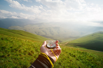 Male hand with a magnetic compass ea against the backdrop of a beautiful landscape at sunset. The...