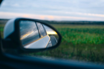 Reflection of the route in the side mirror of the car. Sunset. Summer. Travelling by car.