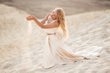Fototapeta na wymiar Portrait of beautiful bride is wearing fashion flying dress sitting on sand in the great desert in Dubai.