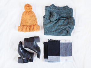Woman's winter outfit accessories with green woolen sweater, black ankle boots, knitted mustard hat and checked scarf. Flat lay. Top view