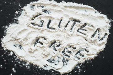 Gluten free message written in flour spread on black slate as background - Allergenic ingredient found in white wheat flour with text in it - Concept image for healthy eating