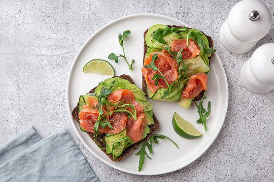 toast with dark rye bread, avocado, smoked salmon and cucumber on white plate,