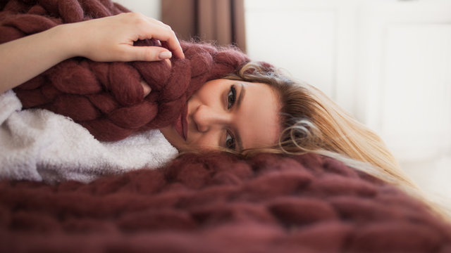 Cute young blonde lying on the bed wrapped in a soft cozy blanket. Warmth and comfort of home