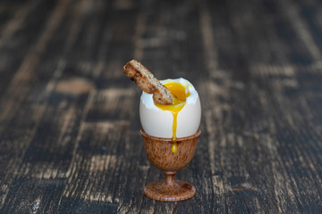 Soft boiled egg in eggcup with slice of toasted bread on wooden table background, closeup