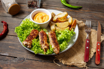 Grilled shish kebab served with fried potatoes and sauce on wooden background