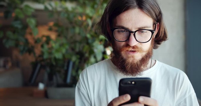 Happy red-bearded male hipster texting on smartphone and smiling, pleasant communication