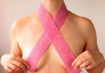 naked girl covers her breast with a pink ribbon - a symbol of breast cancer awareness day, close up, creative