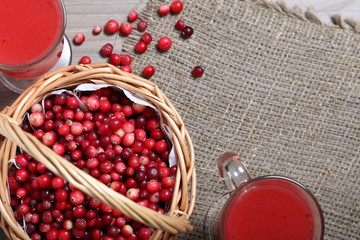 Basket filled with cranberries. It stands on a surface covered with linen cloth. Next to the glasses are cranberry juice. Several berries are scattered on the surface.