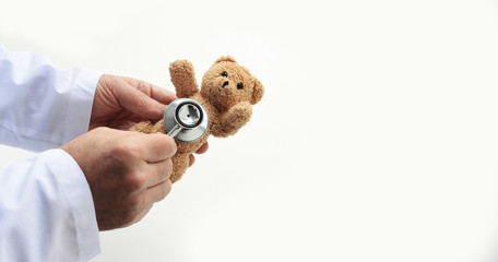 Doctors's hands holding toy teddy bear and putting stethoscope's close to it. Medical help or insurance concept, banner, copy space.