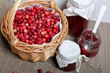 Homemade preserves, cranberry jam in jars. One can is open, it has a teaspoon. Several berries are scattered on the surface.