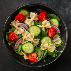 italian pasta salad farfalle, vegetables, mix leaves (tomato, cucumber, onion, lettuce, chard, arugula and more) menu concept. food background. copy space. Top view