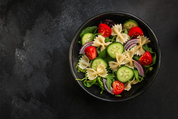 italian pasta salad farfalle, vegetables, mix leaves (tomato, cucumber, onion, lettuce, chard, arugula and more) menu concept. food background. copy space. Top view