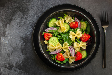 italian pasta salad farfalle, vegetables, mix leaves (tomato, cucumber, onion, lettuce, chard, arugula and more) menu concept. food background. copy space. Top view