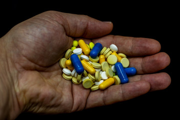 Different colored pharmaceutical pills and capsules on the palm. Dark light, black background.